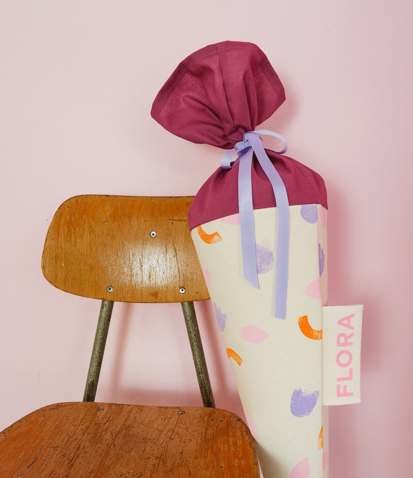 Schultüte aus Stoff mit fröhlichem Blumenmotiv PLAY Flowers zur Einschulung lehnt an einem Kinder-Schultüte