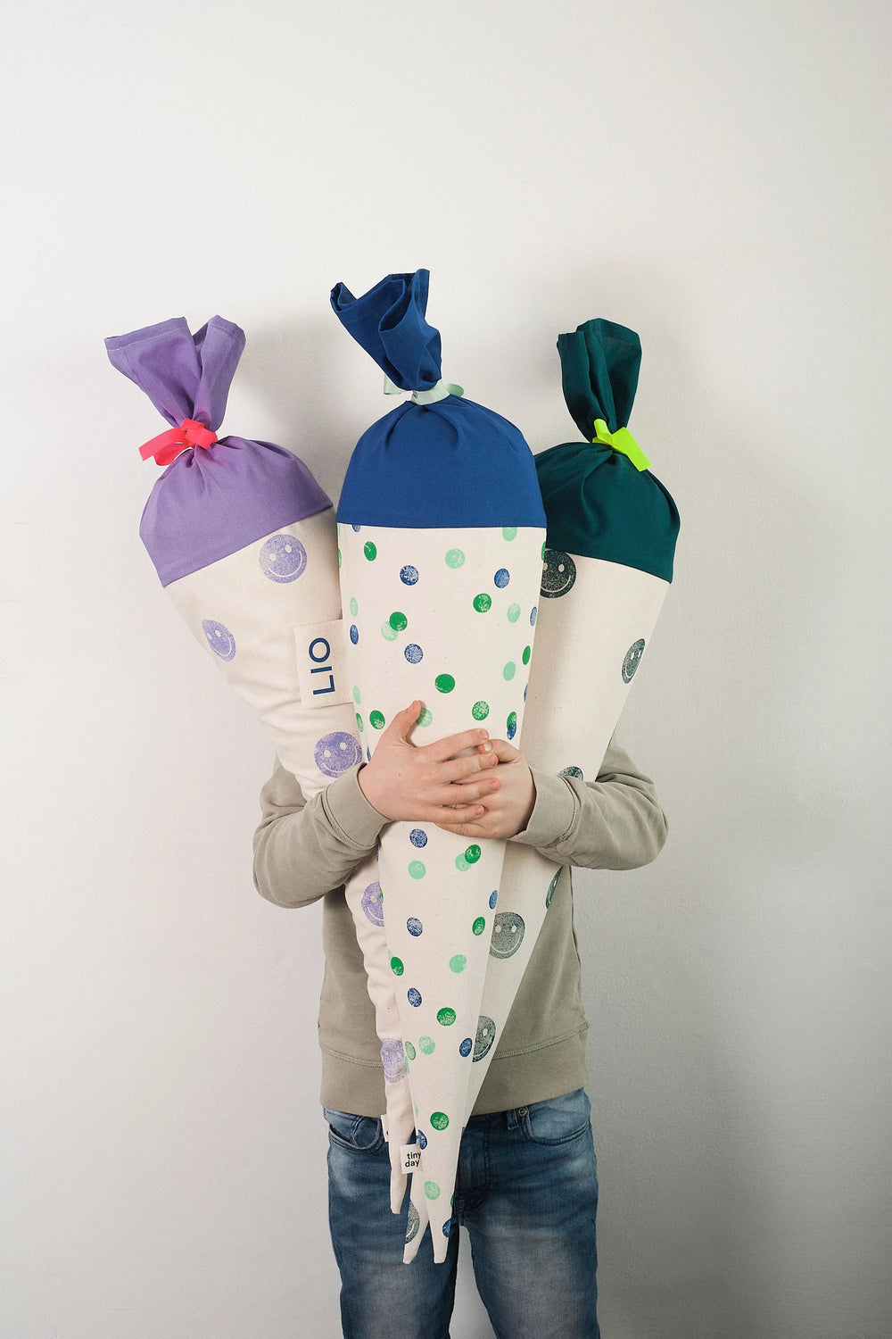 Schultüte aus Stoff zur Einschulung mit Smileys in Türkis. Gestempelt, mit Namenslabel an der Seite sowie frei wählbarer Krempe und Band. Später als Kissen nutzbar.