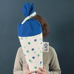 Junge hält eine Schultüte aus Stoff mit Konfetti-blau-Motiv und seitlichem Namenslabel