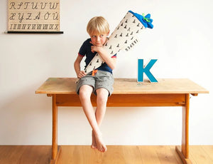 Junge sitzt mit seiner Schultüte Motiv "Tipi" auf einem Schultisch. Im Hintergrund hängt ein ABC-Poster